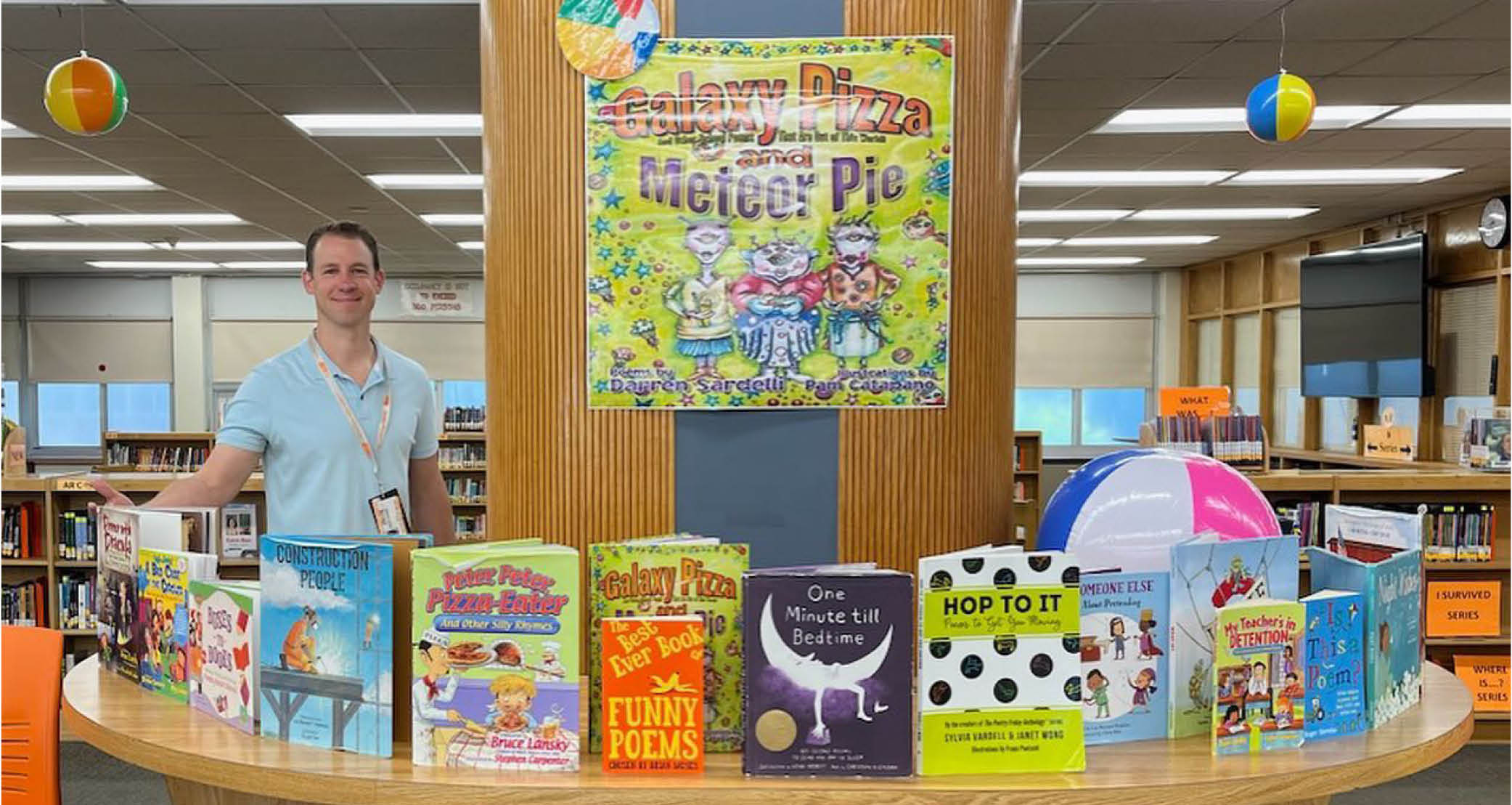 photo of Darren Sardelli standing in a library surrounded by children's books