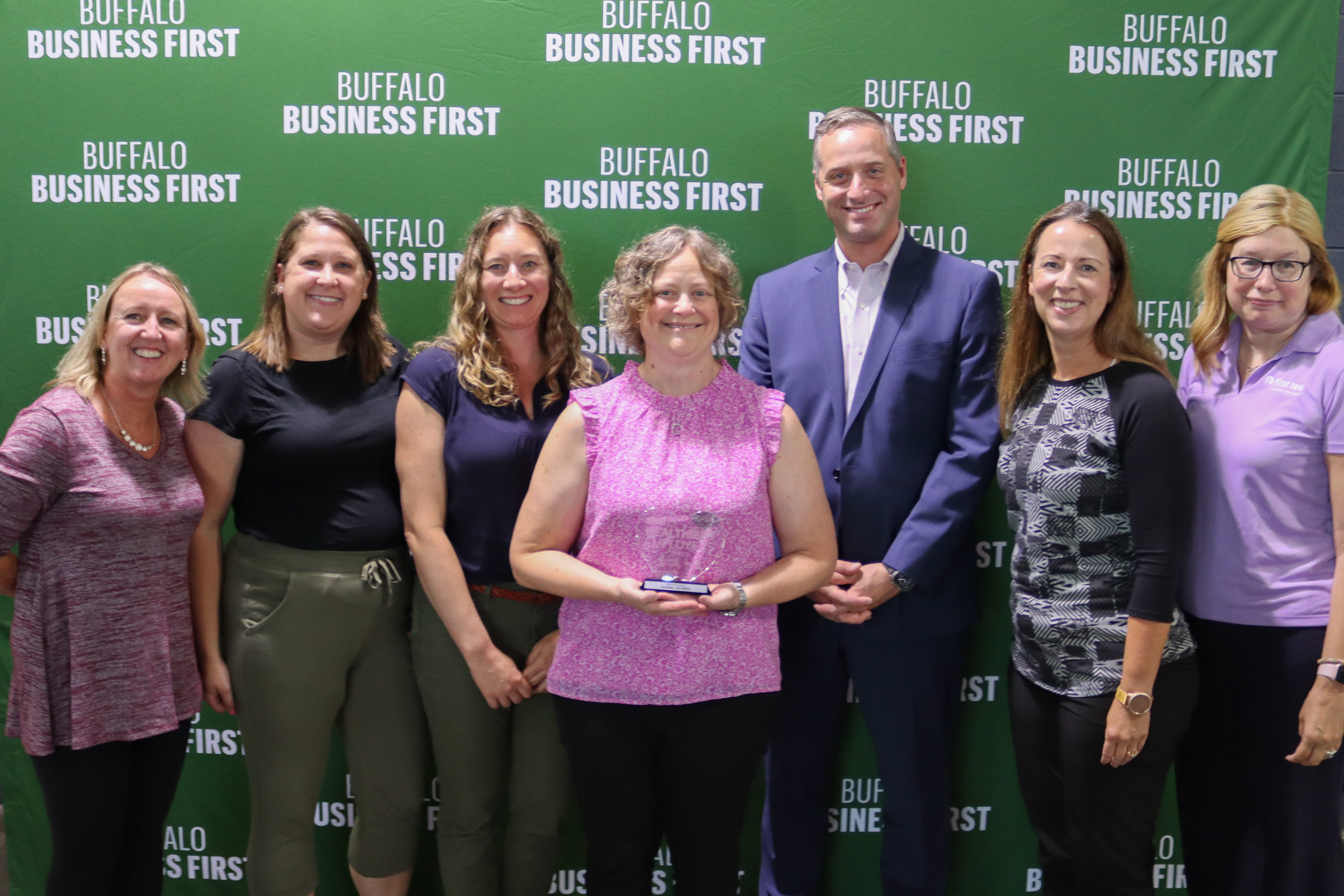 Kate Huber, holding award and Erie 1 BOCES employees pose in front of the Buffalo Business First logo