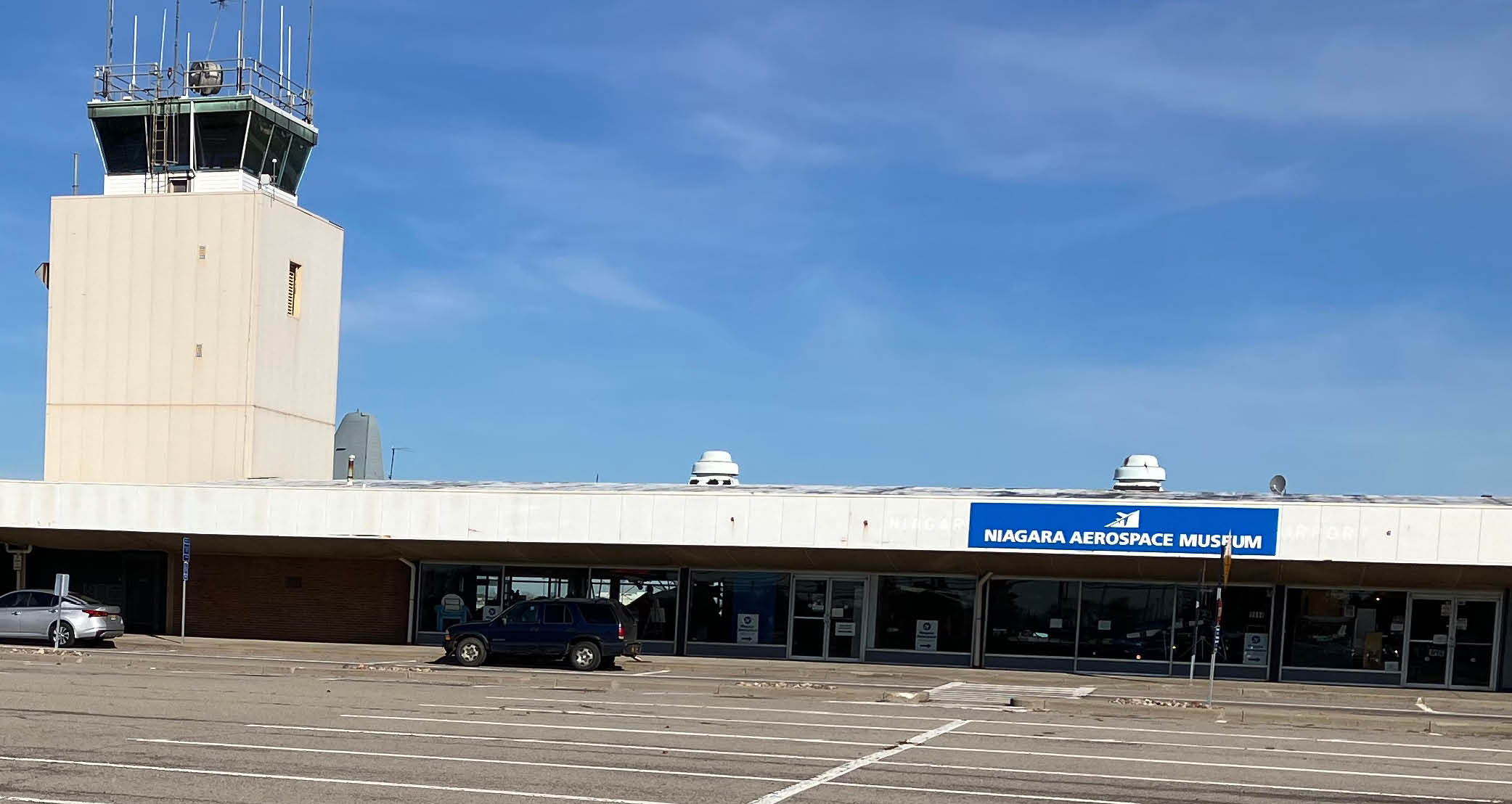 long narrow building with a white front and a sign that reads Niagara aerospace museum