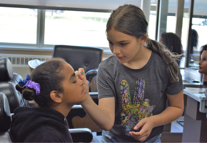 A student applies makeup to a classmate in a classroom